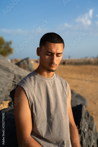 A young man relaxing by some dark rocks on the beach at sunset