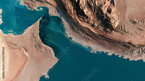 Aerial view of rocky coastline and blue water near desert area with mountains in background