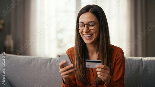 Happy businesswoman using smartphone and bank card at home, mobile banking approval and secure digital payment experience - online finance, cashless shopping and financial technology