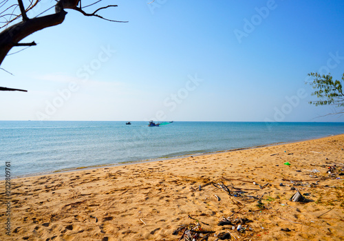 фотографія Trash strewn beac hwith clear turquoise water and fishing boat sailing in distance on sunny day