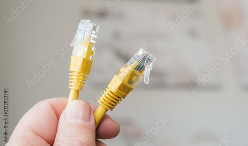 Hand holding two yellow ethernet network cables with RJ45 connectors.