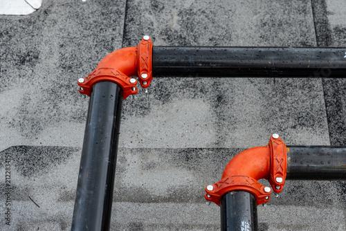 Photo of HVAC heating and cooling black metal pipes with red elbow joints that are supported by metal frames on a flat rooftop.