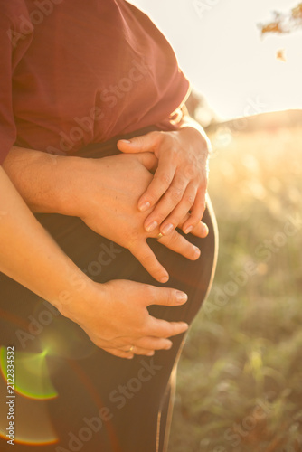 close-up of a pregnant woman's belly with both parents gently resting their hands on it, warm natural daylight