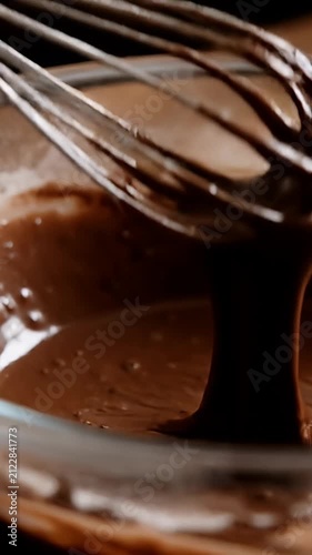 Hand whisking rich chocolate batter in a glass bowl.