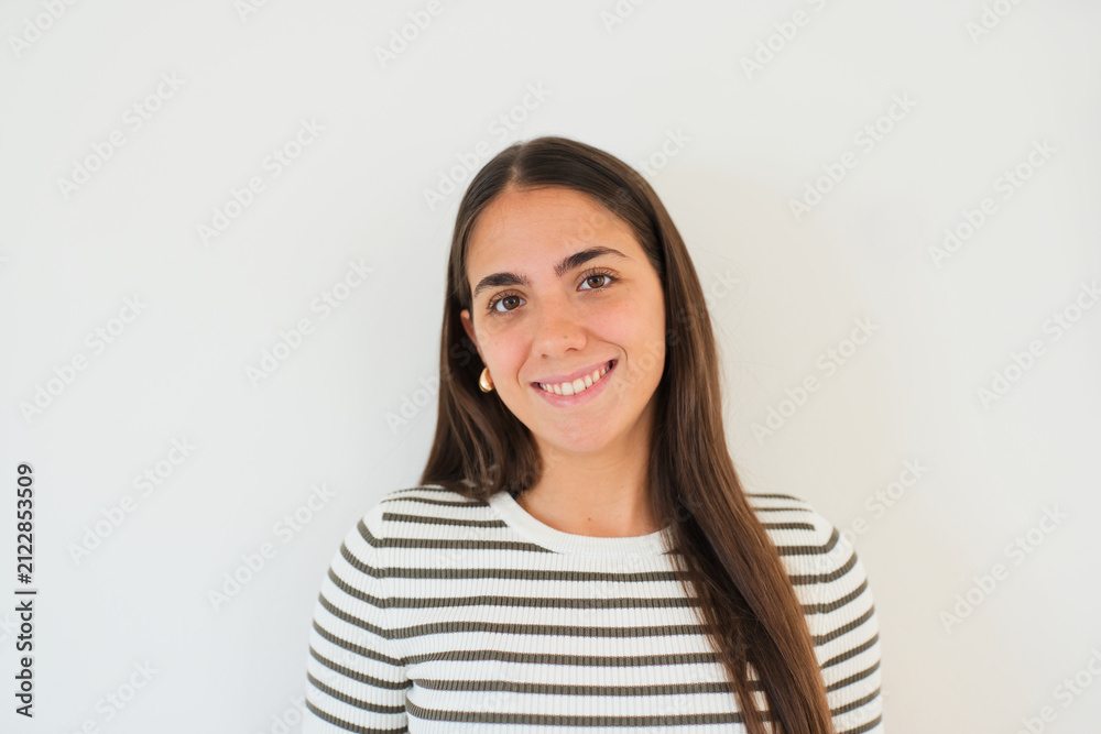 Obraz premium Smiling young woman wearing a striped sweater poses for a natural headshot against a clean white background, conveying warmth, confidence and approachability in a simple lifestyle portrait.