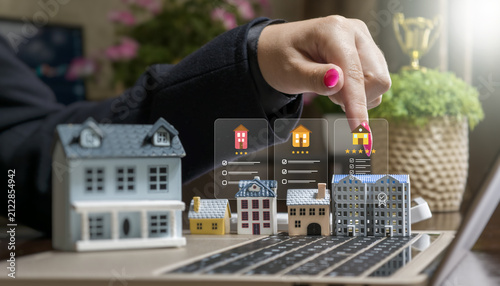 Online real estate search and property management with digital icons over miniature houses on a laptop keyboard.