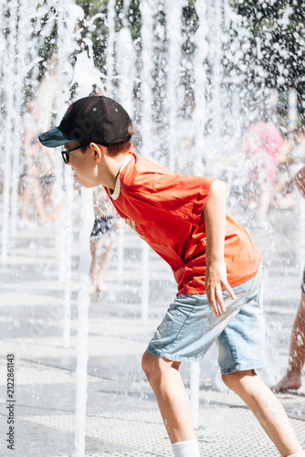 Boy playing with splashing water at an outdoor city fountain during a sunny summer day, active childhood recreation