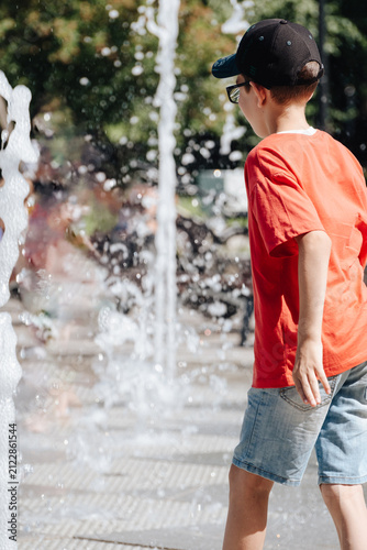 Boy playing with splashing water at an outdoor city fountain during a sunny summer day, active childhood recreation