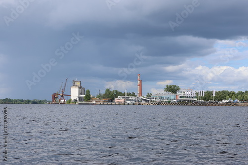 Obraz na plátně A wide view from the water showing an industrial area and cargo port along a river bank