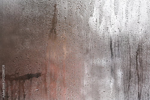 glass with condensation and dripping water lines, glass showing humidity and wet surface texture, blurred view behind window, climate concept, rain and moisture, abstract background, closeup detail