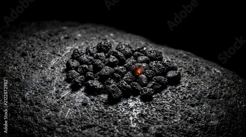A single glowing ember shines among dark volcanic stones, symbolizing hope, individuality, and inner strength amidst obscurity.