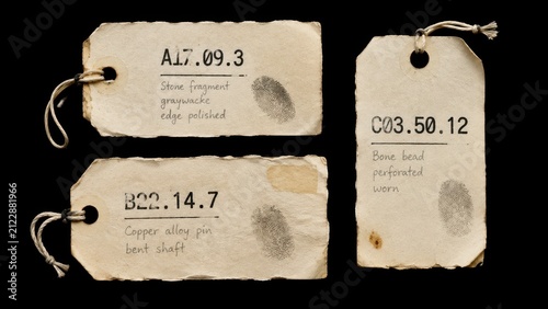 Three aged museum artifact labels with string on black background