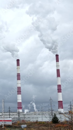 Two tall. Red and white industrial chimneys billowing thick smoke and steam into a grey. Overcast sky. Highlighting the concepts of air pollution and global warming from fossil fuel energy production