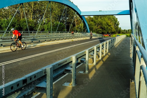 A cyclist in a red jersey crosses a bridge