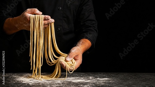 Chef stretching fresh handmade noodles over a floured table