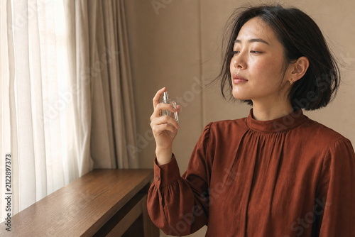 カーテンのそばで香水をまとうショートヘアの女性