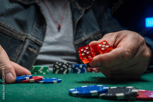 Obraz na płótnie A person holds two red dice in one hand while poker chips are arranged on a green table