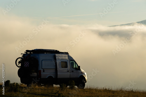 Camper van parked above clouds at sunrise