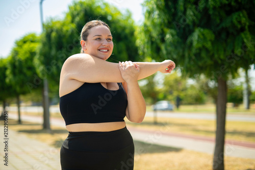 Foto Plus size woman stretching arm outdoors in park