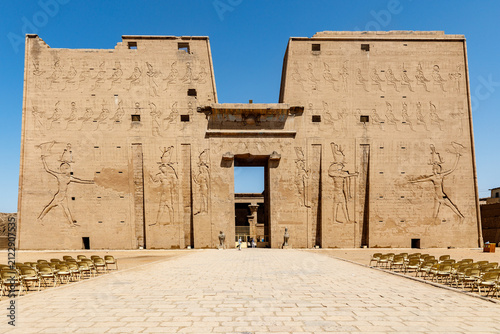 The Temple of Edfu, an ancient Egyptian Ptolemaic temple, stands under a clear blue sky with rows of chairs in the foreground.