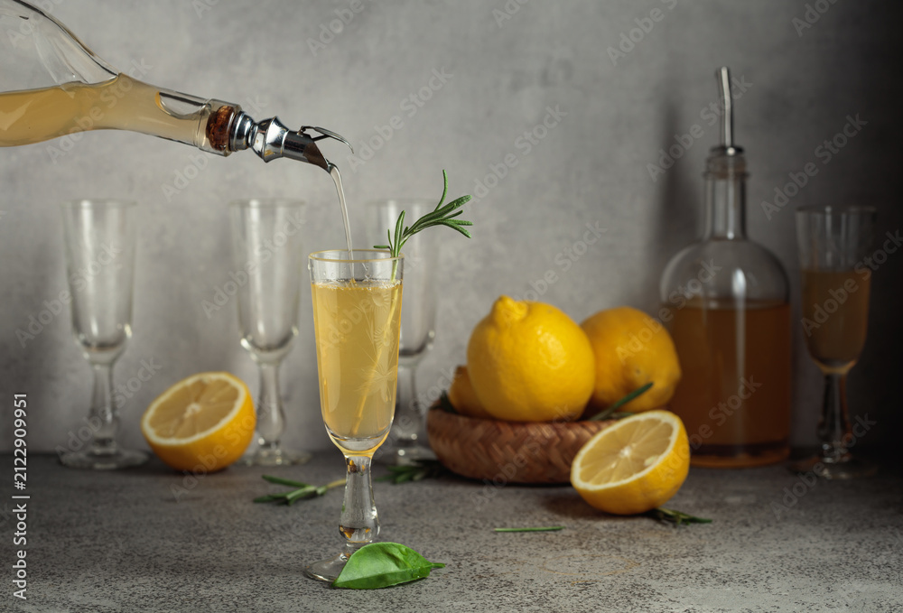 Obraz premium Italian liqueur Limoncello with fresh lemons and rosemary branches on a gray stone table.