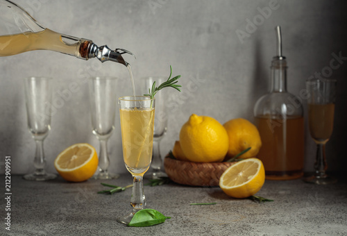 Italian liqueur Limoncello with fresh lemons and rosemary branches on a gray stone table.