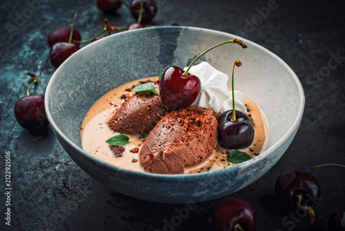 Modern dessert - dark black chocolate mousse au chocolat in vanilla sauce with black sweet cherries and meringues served as close-up in a design bowl