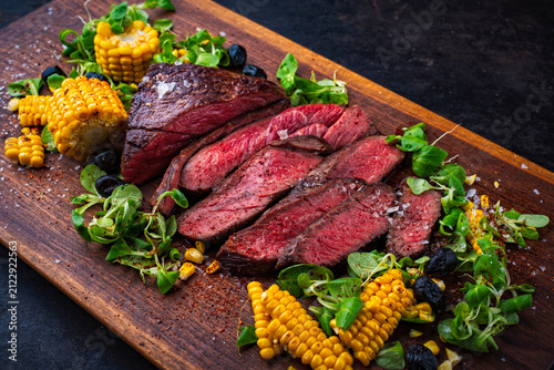 BBQ roasted under-blade steak chuck roast, denver cut beef steak with grilled vegetables, maiz corn, green salad served as close-up on a wooden board