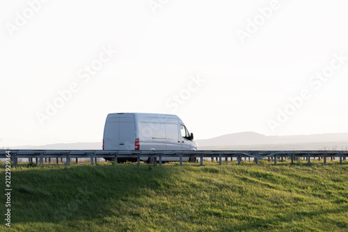 White modern delivery small shipment cargo courier van moving fast on motorway road to city urban suburb.	