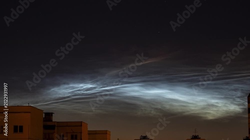 Rare noctilucent clouds illuminating the night sky above residential rooftops at dusk
