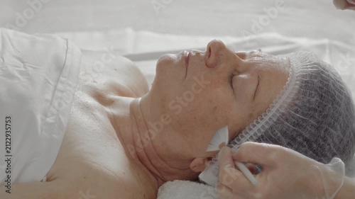 Cosmetologist applies a rejuvenating mask on the face of an elderly woman