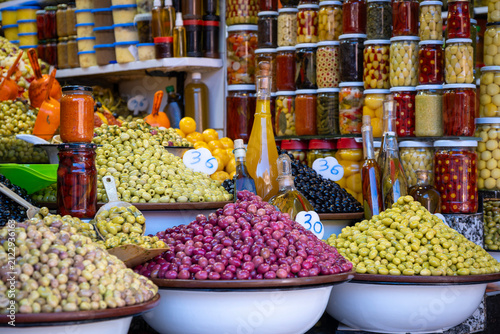 large variety of green and purple olives piled in bowls with jars of pickled vegetables and oil at market stall in Marrakech Morocco,street pickle stand