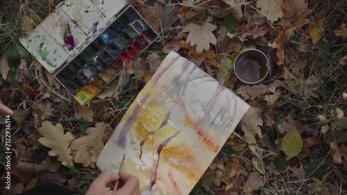 The artist paints a forest landscape on the ground among fallen autumn leaves