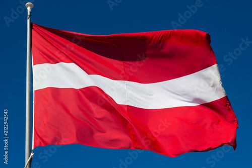 Konstfotografi Red and white flag of Latvia waving against a clear blue sky, showcasing the nat