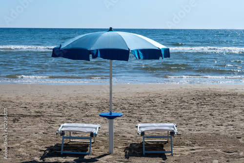 Fotografie Blue beach umbrellas and empty sunbeds line on sandy shore near Sperlonga, Italy