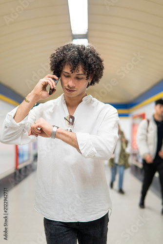 Man check wristwatch while talk on smartphone in subway