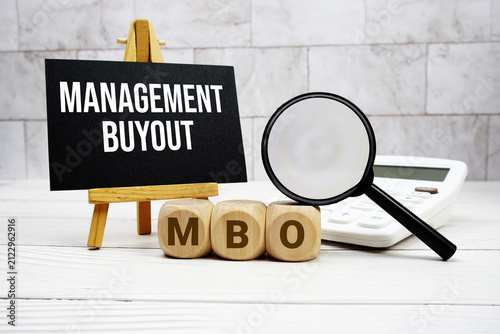 MBO Management Buyout text with calculator magnifying glass and on wooden background