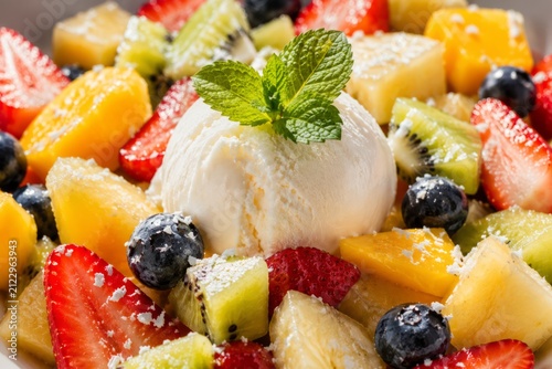 Macro close-up of creamy vanilla ice cream served with fresh tropical fruit salad, berries and mint for a refreshing summer dessert
