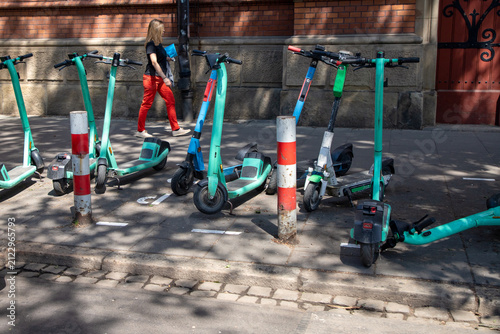 E-scooters, rental option in cities. To rent and park. They are parked along a city street, Dockless bike-share parking,  Fleets have faced criticism for blocking pavements and impeding pedestrians.  