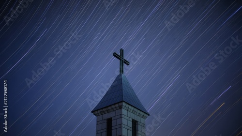 Silhouette of a church cross steeple under a starry night sky with diagonal star trails