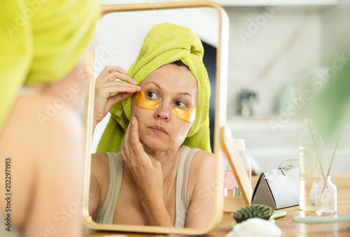 Foto Serene woman with towel turban on head after taking shower applying gold under-e
