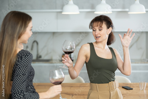 Bild auf Leinwand Two joyful middle-aged women dancing together at the table with wineglasses in l