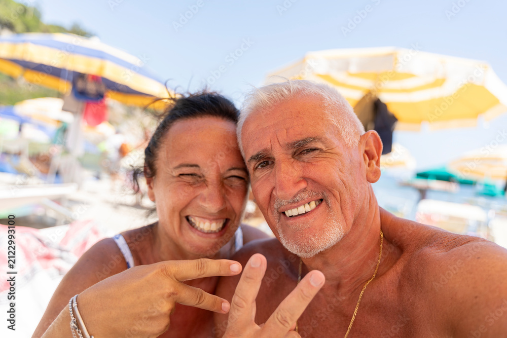 Naklejka premium Senior couple enjoying summer beach vacation, smiling and making peace sign