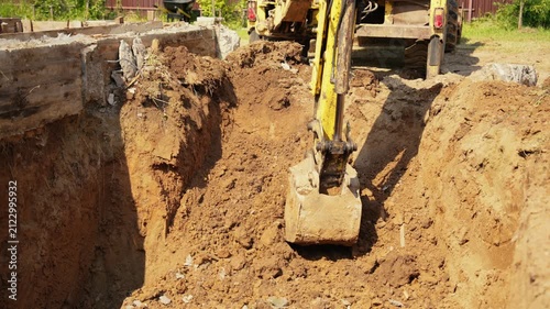 Yellow excavator machinery filling a large pit with soil during earthworks on a sunny construction site, preparing the ground for the foundation of a new building in slow motion
