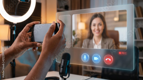 Hands Holding Smartphone Interacting with Futuristic Hologram Video Call Interface, AI Virtual Meeting, Online Interview, and Content Creation Technology Concept