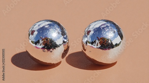 Two Spherical Silver Magnets Displaying Reflected Light on a Plain Background