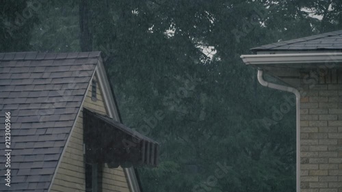 Dramatic slow motion rainfall striking the roofs, gutters, and awnings of neighboring suburban homes during a heavy summer rainstorm. 15275  