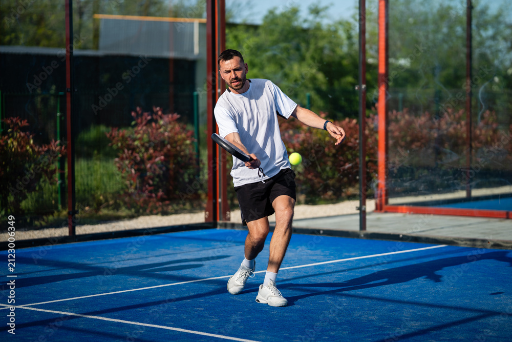 Obraz premium Male padel player hitting a yellow ball on blue court