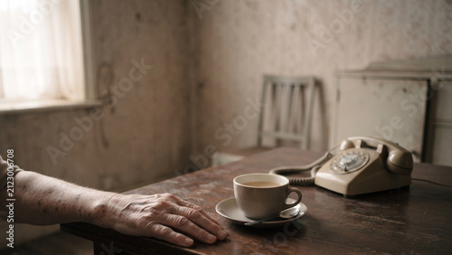 Elderly Person's Hand Resting on a Wooden Table with Tea and Rotary Telephone