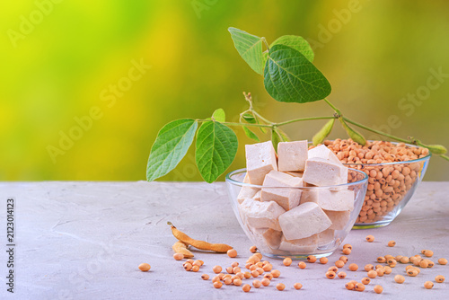 Tofu, also known as bean curd, diced in glass bowl against the background of a branch young green pods soybean, closeup with space for text